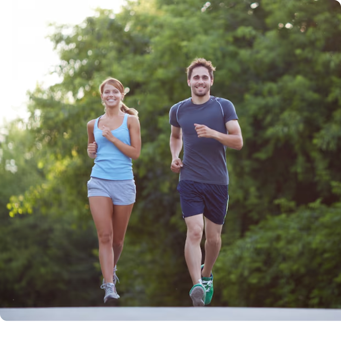 Two people jogging happily outdoors on a path surrounded by greenery.