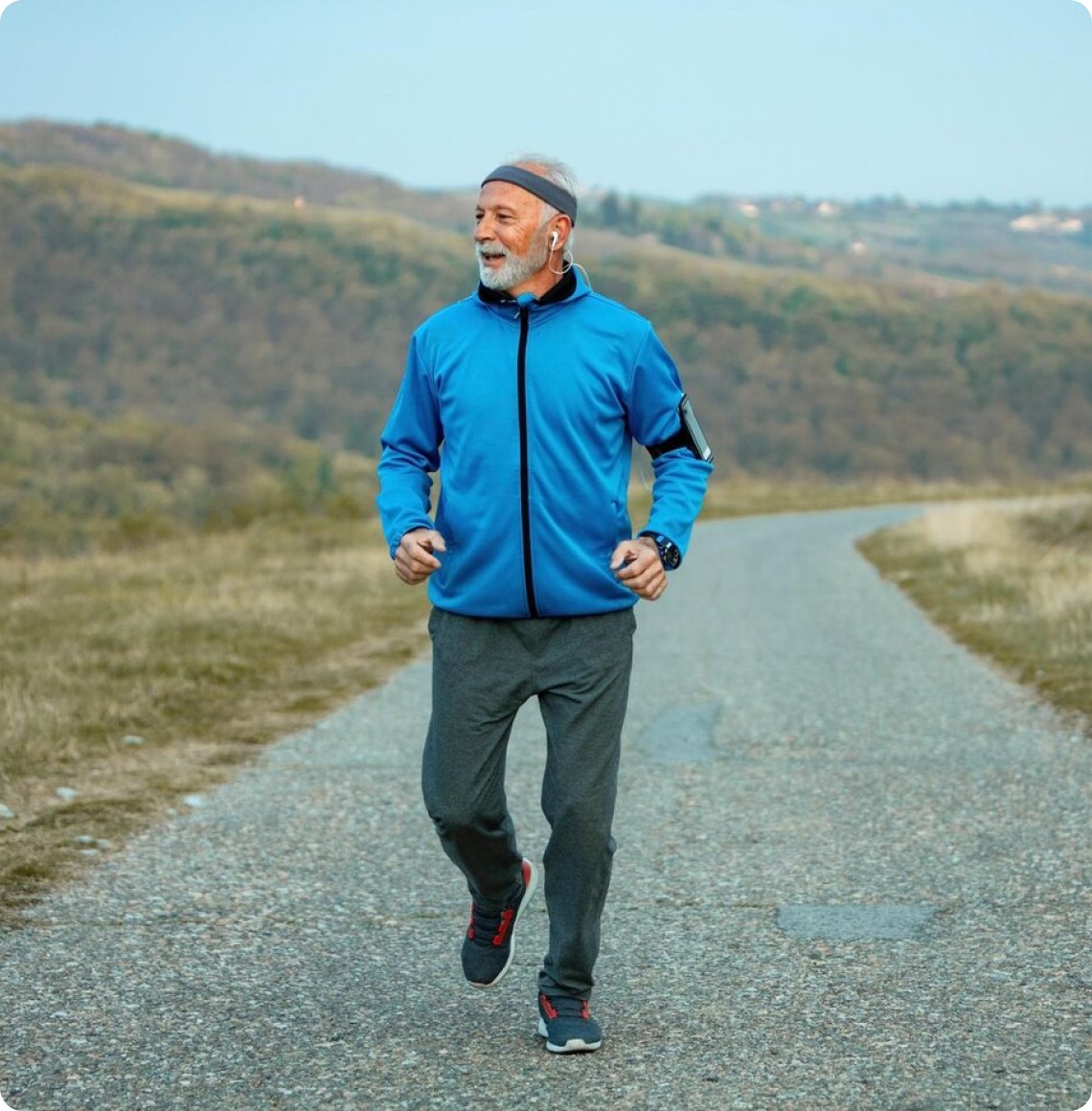 An older man jogging outdoors on a paved path with scenic nature in the background.