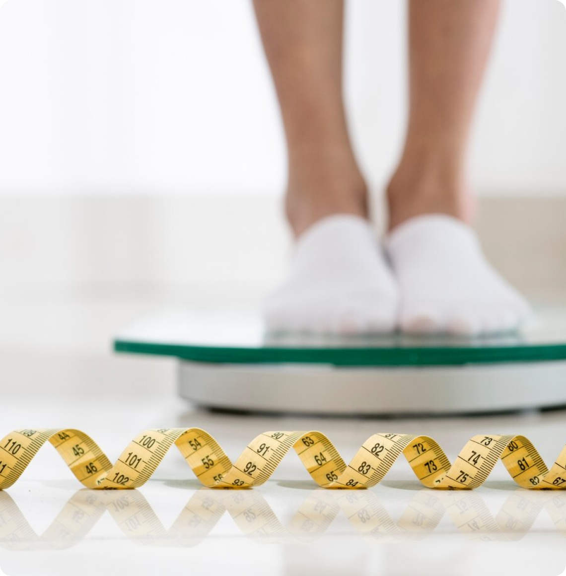 A person standing on a scale with a measuring tape showing decreasing sizes in the foreground.
