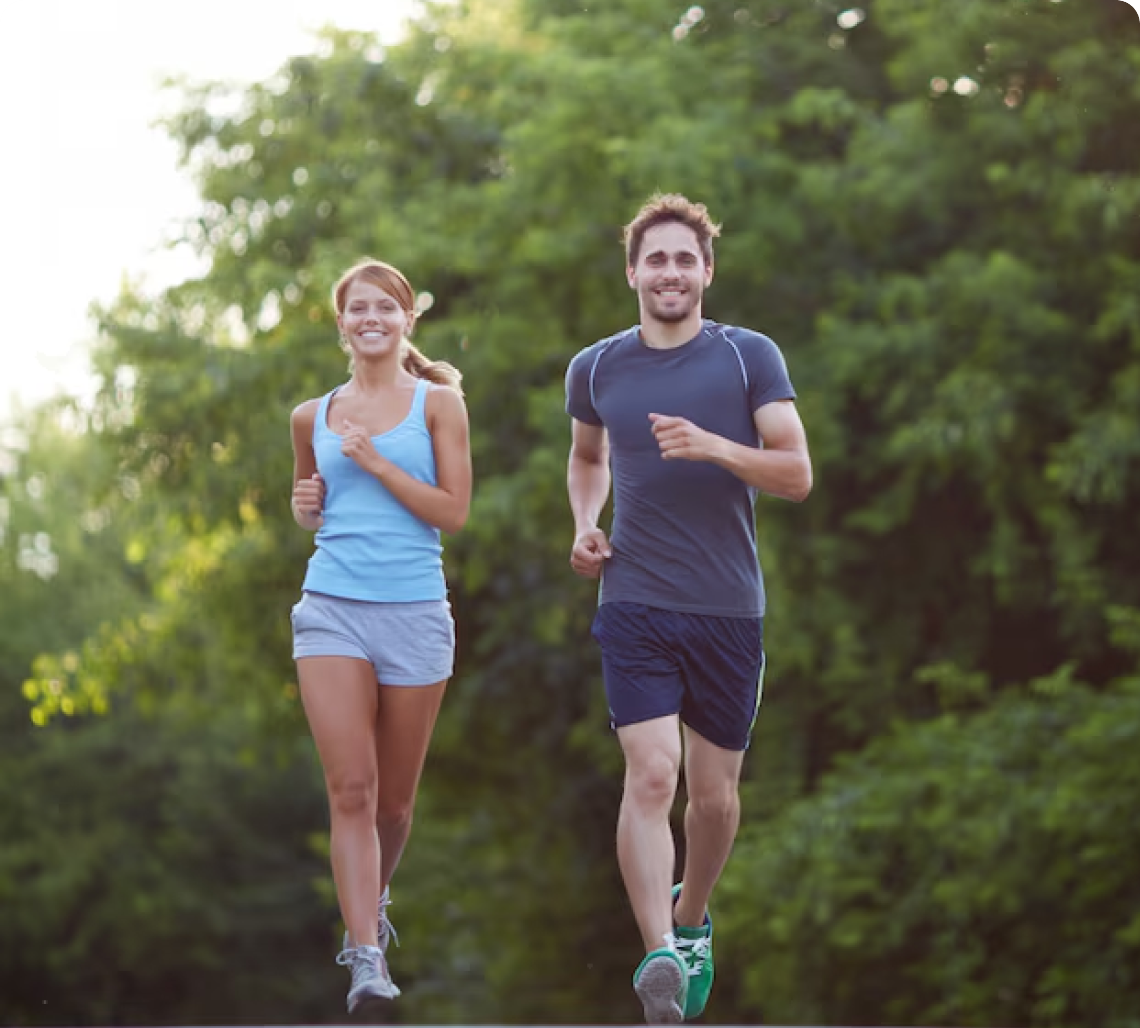 A couple jogging happily in a lush green park setting, smiling and exercising outdoors.