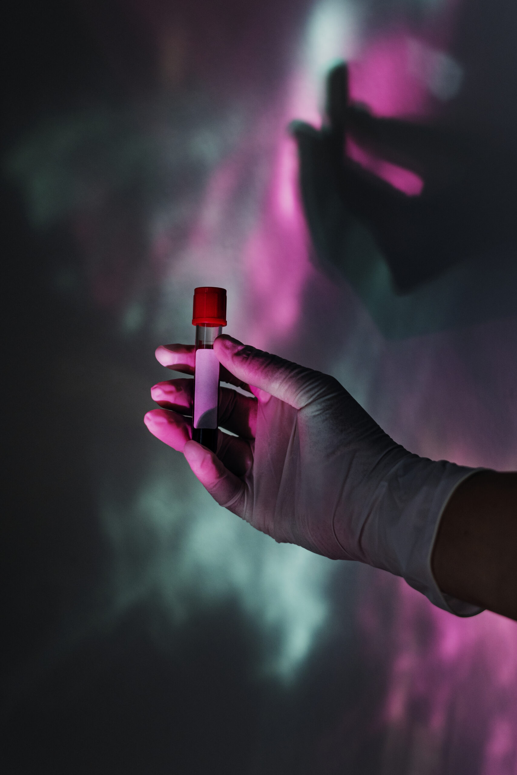 A gloved hand holding a small vial with a red cap against a colorful, blurred background.