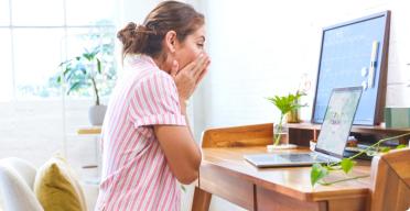 A woman sitting at a desk covering her mouth, appearing unwell near an open laptop.