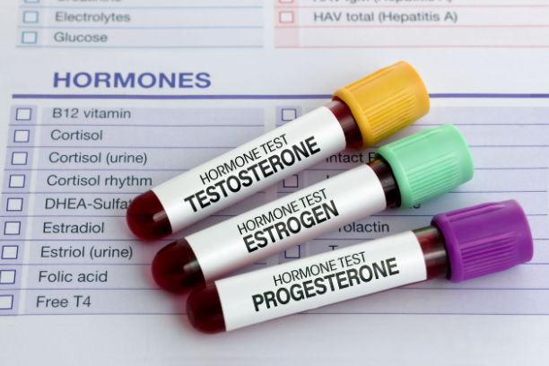 Hormone blood test tubes labeled testosterone, estrogen, and progesterone placed near a lab form.