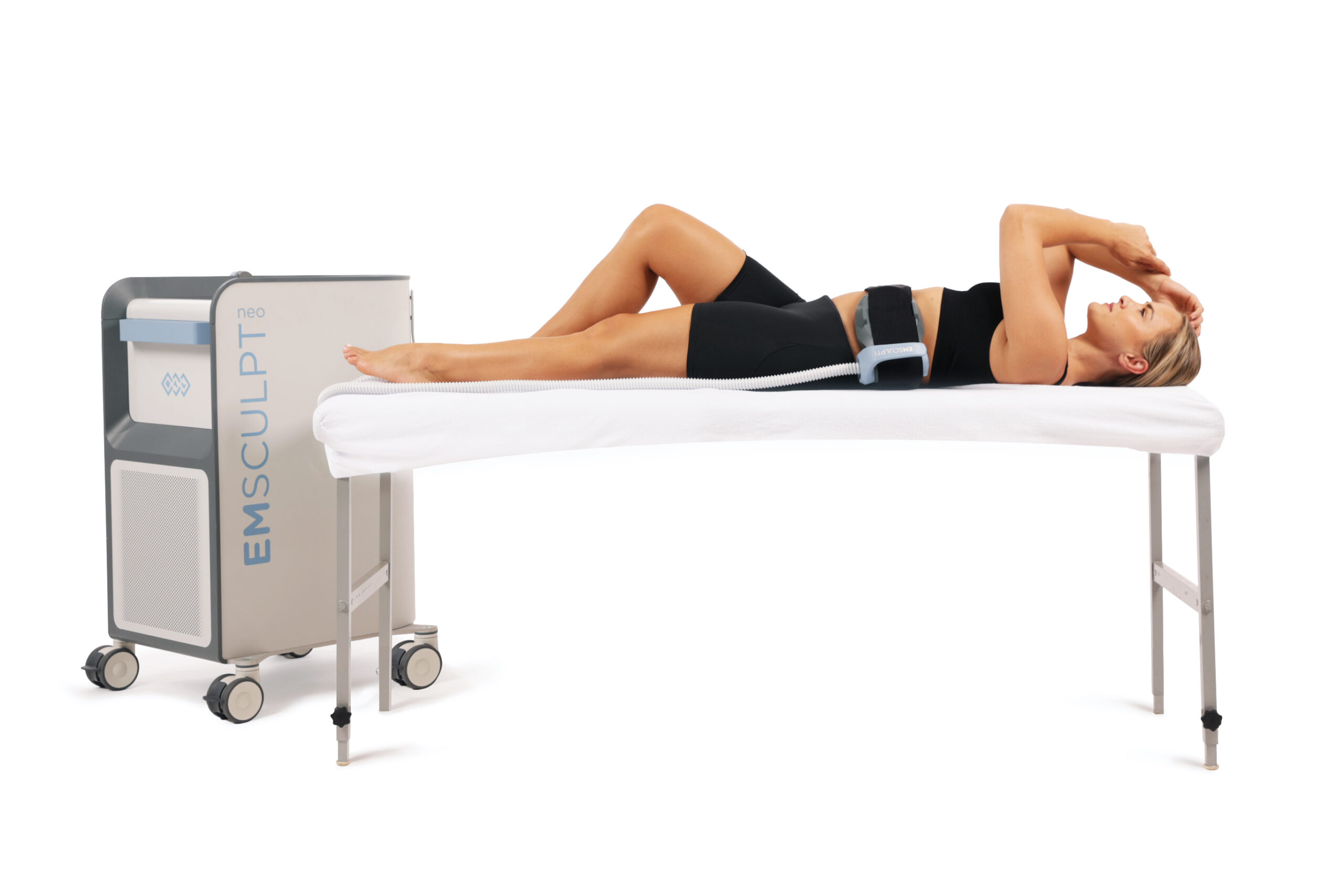 A woman undergoing EMSculpt body contouring treatment on a specialized table with attached device.