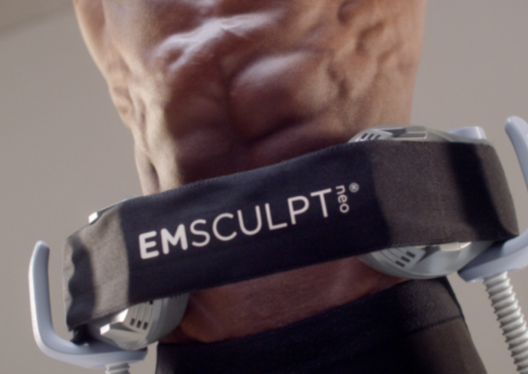Person holding EMSculpt Neo device for muscle toning during exercise.