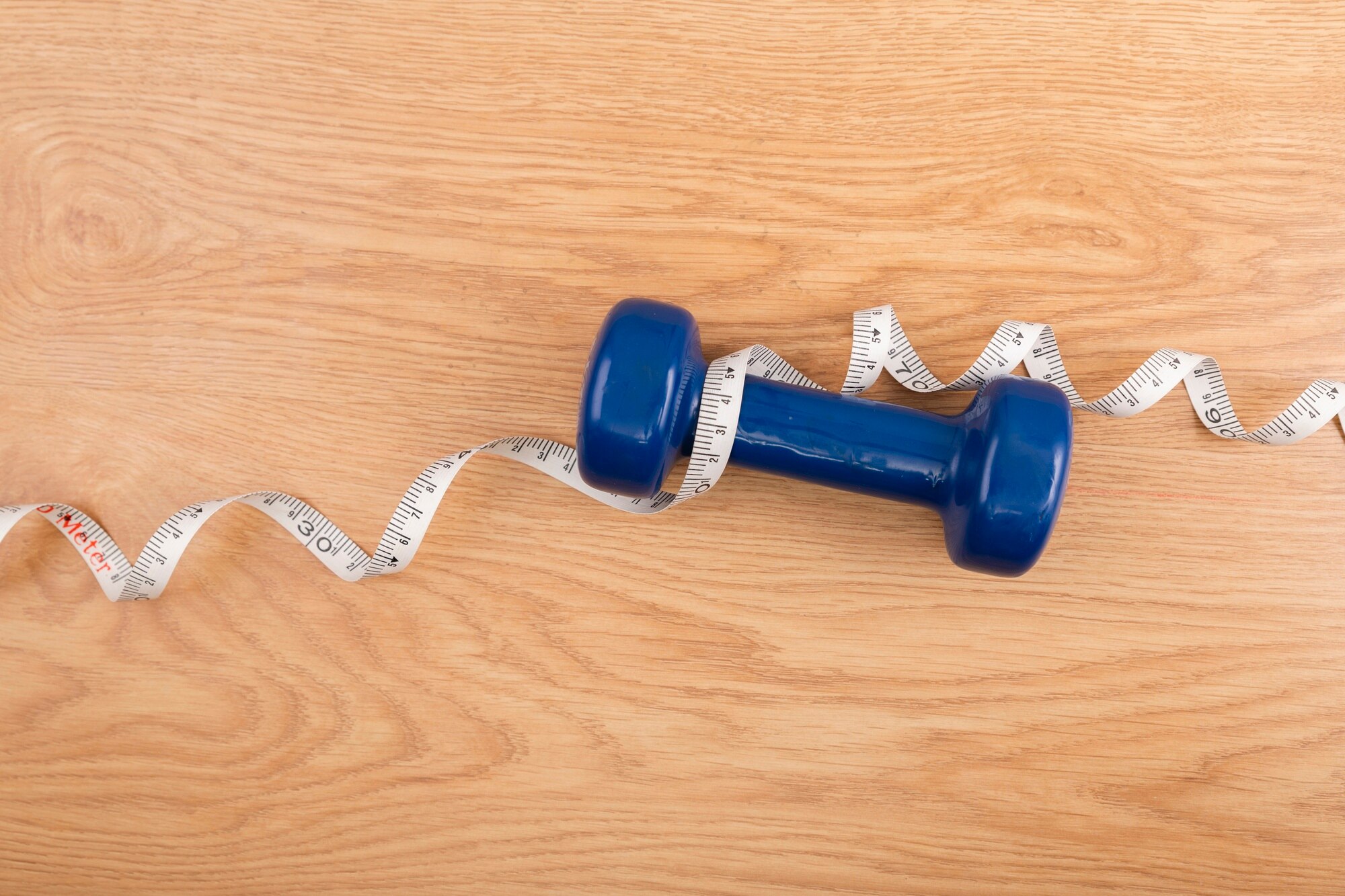 Dumbbell wrapped with a measuring tape on wooden surface.